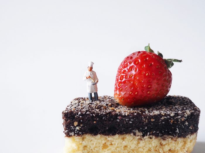 Close up miniature people on chocolate cake with fresh strawberry on top,cooking and decoration concept.