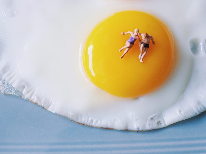 Close up couple lover miniature people laying on yolk of fire egg.