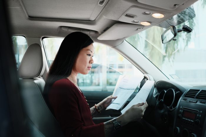 Chinese female manager working in car. Successful Asian businesswoman using laptop computer and looking at paperwork.