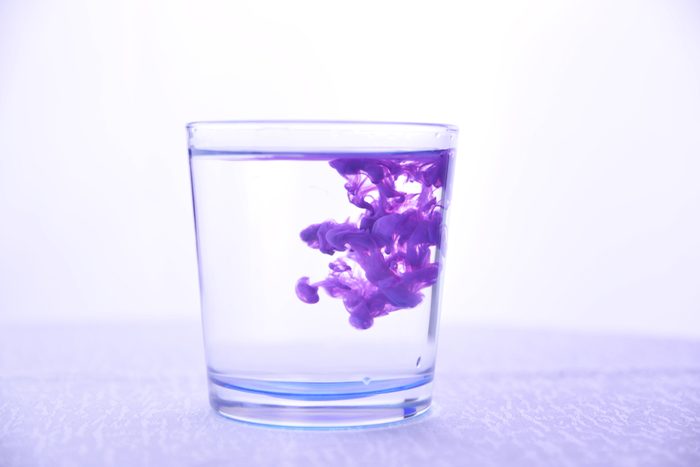 Glass with water on a white background with purple paint.