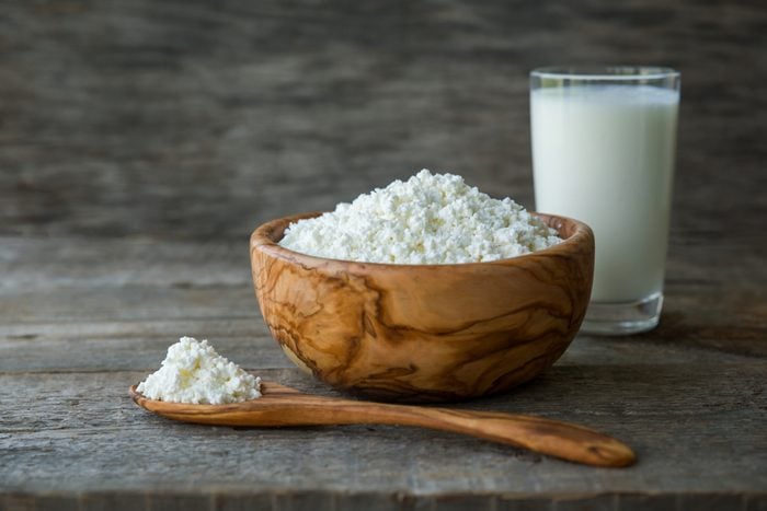 Fresh cottage cheese in a wooden bowl with a spoon with a glass of milk on a wooden old background