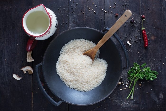 rice in a frying pan with parsley , pepper and water on the dark background