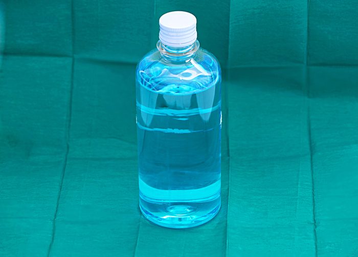 blue ethyl alcohol liquid in plastic transparent bottle on green surgery background