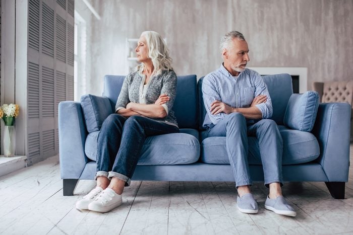 Senior couple at home. Handsome old man and attractive old woman are having relationship problems. Sitting on sofa together and looking to opposite sides.