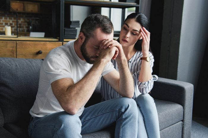 depressed young couple sitting on couch at home after quarrel and looking away