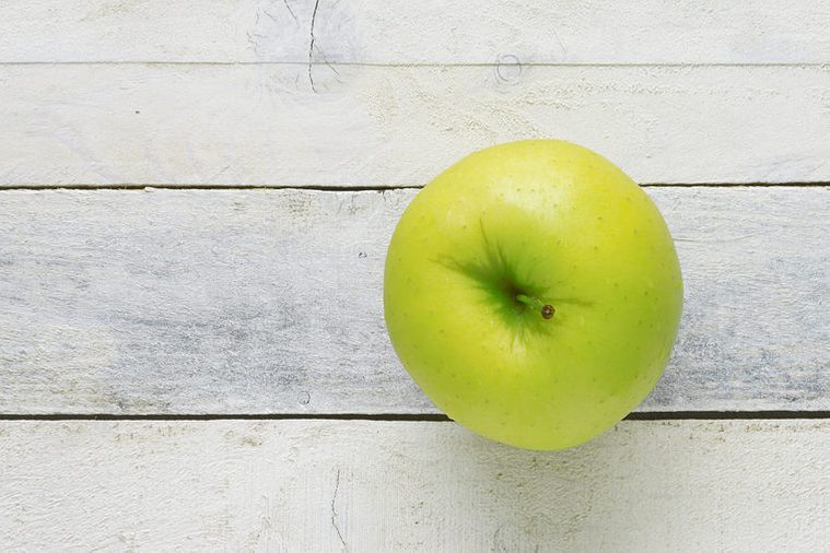 A green apple on a white wooden table. Top view. Empty copy space for editor's text.