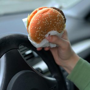 Close up of driver's hand at the wheel while eating food in the traffic