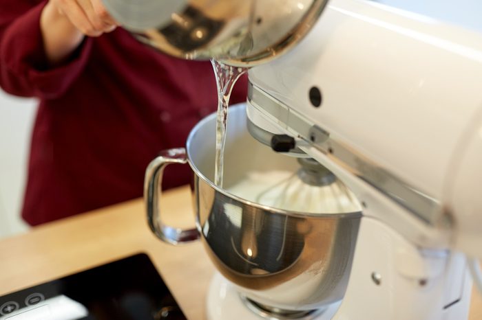cooking, food and kitchen appliances concept - chef pouring ingredient from pot into electric mixer bowl