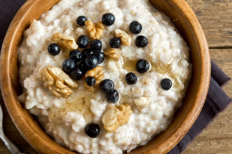 Oatmeal porridge with walnuts, blueberries and honey in wooden bowl with copy space - healthy rustic breakfast
