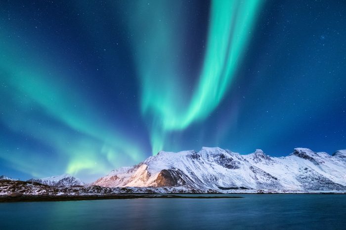 Aurora borealis on the Lofoten islands, Norway. Green northern lights above mountains. Night sky with polar lights. Night winter landscape with aurora and reflection on the water surface. Natural back