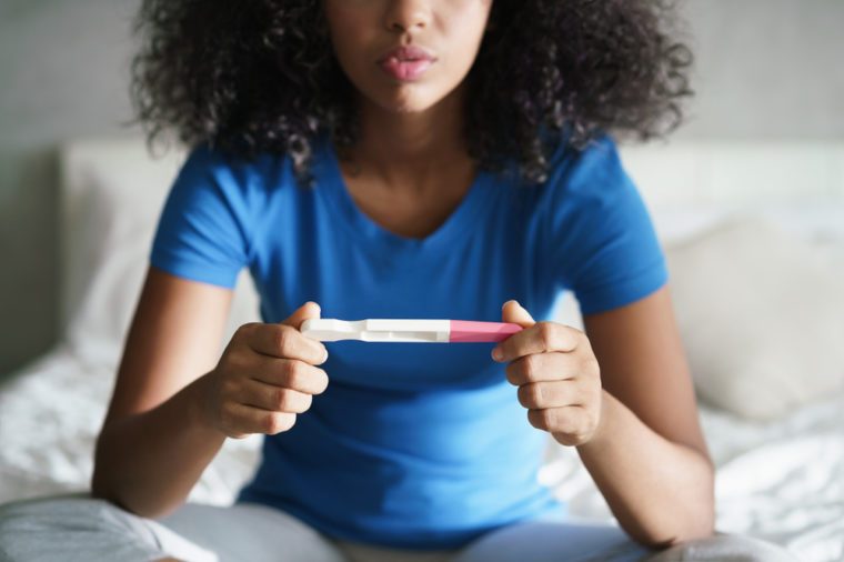 Disappointed hispanic girl getting unexpected result from pregnancy test kit. Sad young latina woman sitting alone on her bed.