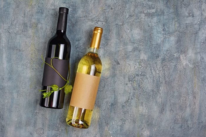 Flat lay of lying organic wine bottles with empty labels and green vine on gray concrete background
