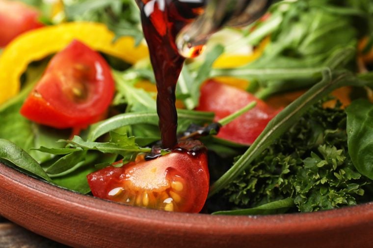 Pouring balsamic vinegar to fresh vegetable salad on plate, closeup