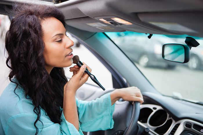 Attractive young woman touching up her make up in a Car looking in the rear view mirror