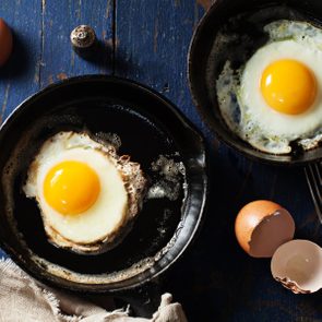 Old-fashioned fried eggs in cast-iron skillets on wooden background