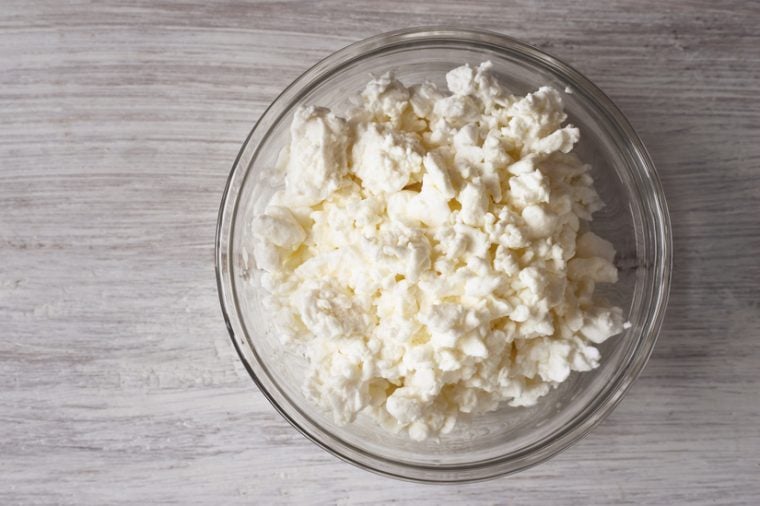Cottage cheese in a glass bowl on a white wooden table