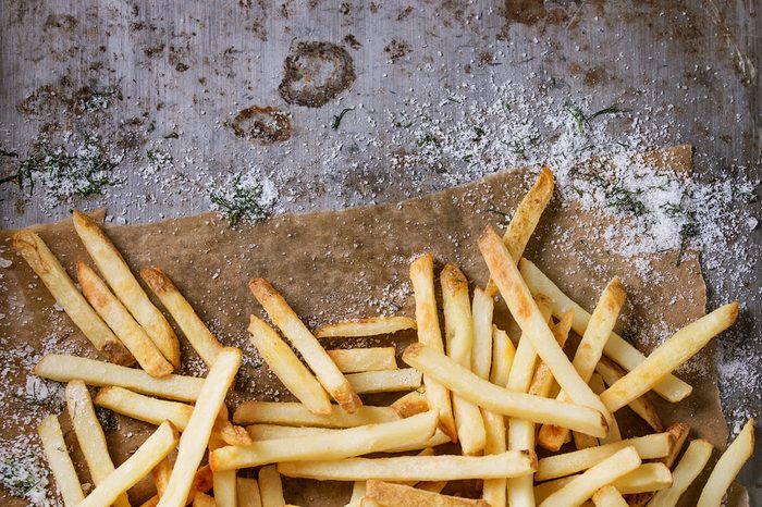 Fast food french fries potatoes with skin served with salt and herbs on baking paper over old rusty metal background. Top view, space for text