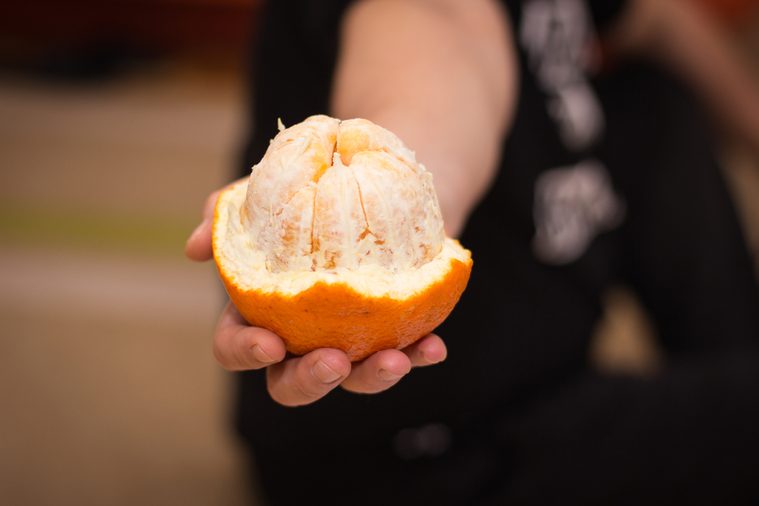 Orange to the half peeled in human hand.