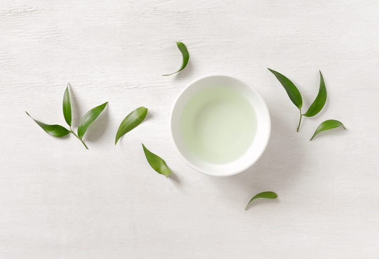 Tea concept, white cup with tea surrounded with green tea leaves, view from above