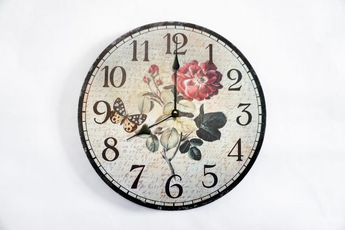 Vintage clock hanging on white wall shows eight o’clock