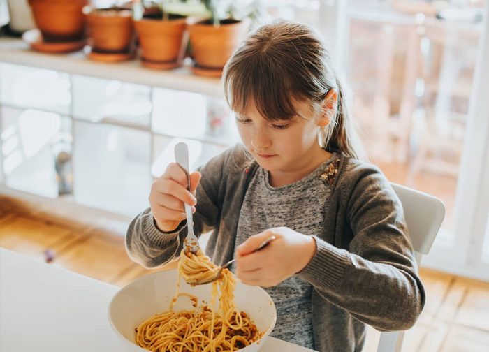 Little kid girl eating spaghetti bolognese at home for lunch