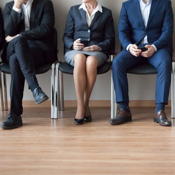 Legs of diverse job applicants sitting on office chairs in corridor waiting in turn for interview, feet of work candidates expect in queue for hiring or employment talk. Recruitment concept