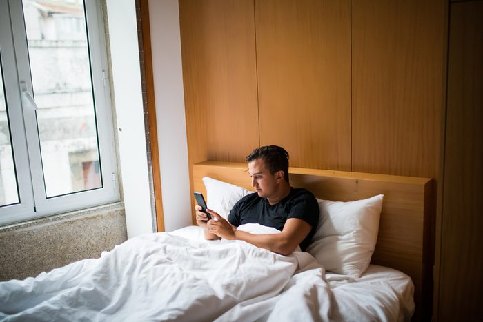 Young man in bed waking up with cellphone at home