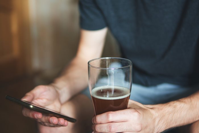 Partial view of a person with alcohol and a phone. Drinks and rests at home