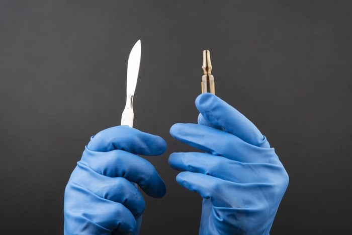 Medical scalpel and vial for injection in hands wearing blue gloves