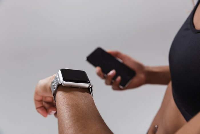 Close up of a young african sportswoman syncing mobile phone with smart watch isolated over gray background