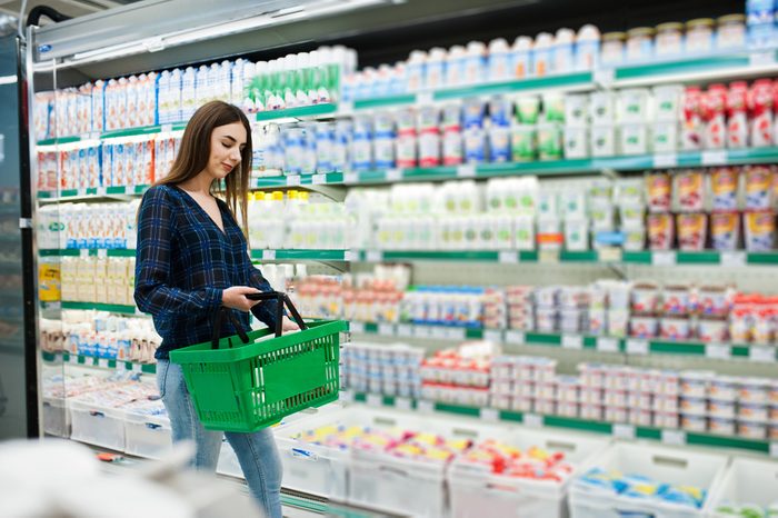 Shopping woman looking at the shelves in the supermarket. Portrait of a young girl in a market store holding green shop basket and milk production.