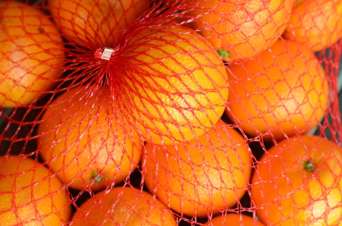 Fresh orange oranges in plastic netting In Market. Food background texture