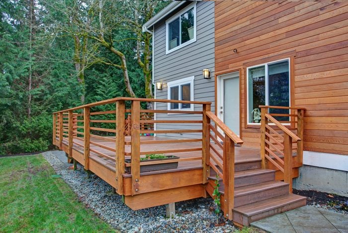 Charming newly renovated home exterior, natural wood and grey siding create a beautiful curb appeal. Detail view of a nice walk out deck with wooden handrails.