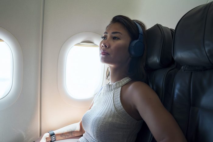 Concerned or saddened woman on an airplane. sitting in a window seat with headphones on.