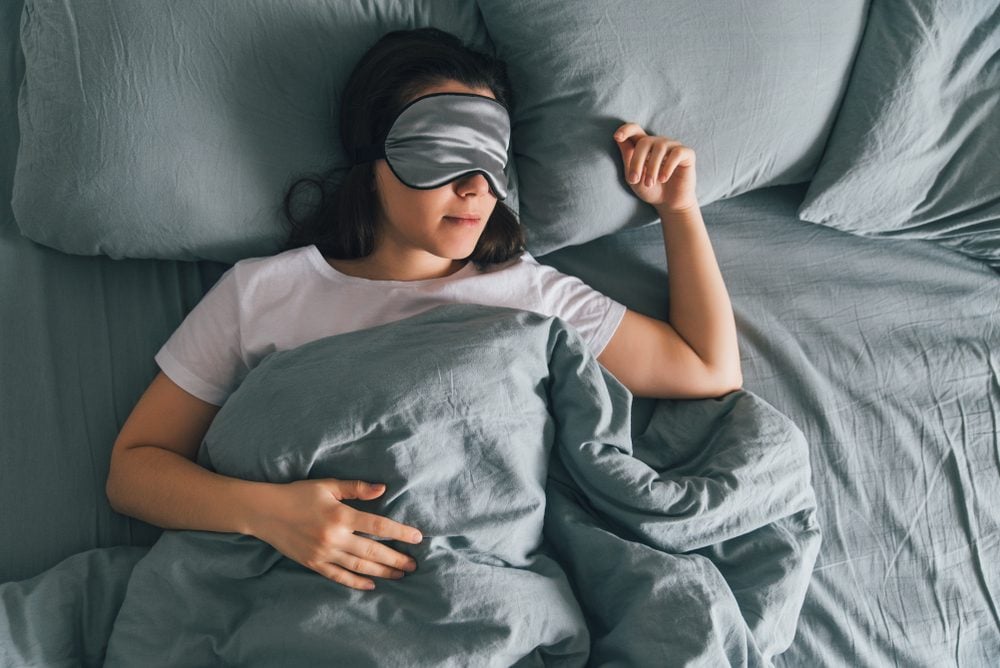 donna dorme con benda sull'occhio in letto grigio. copy space