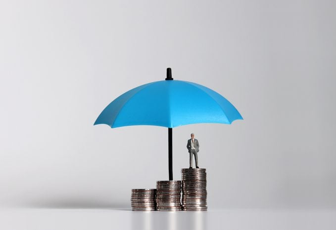 Miniature businessman standing on a pile of coins with umbrella.