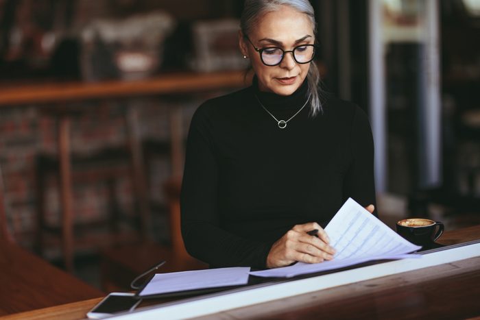 Mature woman sitting in a restaurant and doing some paperwork. Female sitting in cafe with a coffee reading some papers.