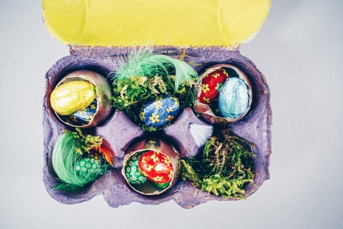 Simple Easter decoration with chocolate eggs , golden painted egg shells and natural materials in egg carton painted violet and yellow. View from above, copy space.