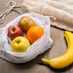 Zero waste, plastic free recycled textile produce bag for carrying fruit (apple, orange, pear and a banana) or vegetables, a wooden surface. Bags are made with a sewing machine out of old curtains.