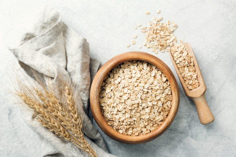 Rolled oats in wooden bowl and ears of wheat on grey background. Table top view. Healthy eating, healthy lifestyle, gluten free diet concept
