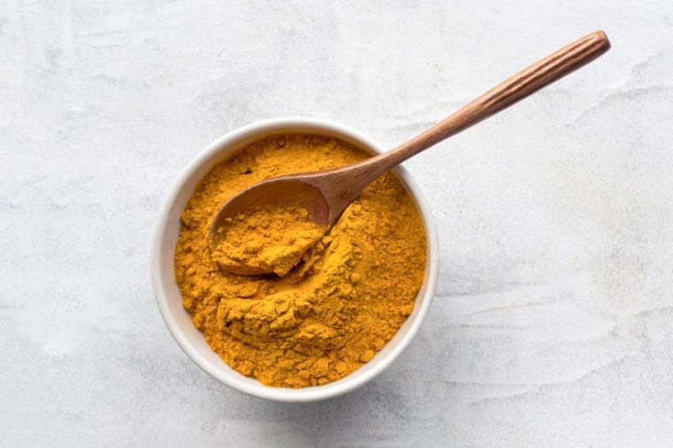 Golden turmeric powder and wooden spoon. Concrete background. Traditional indian spice. Top view.
