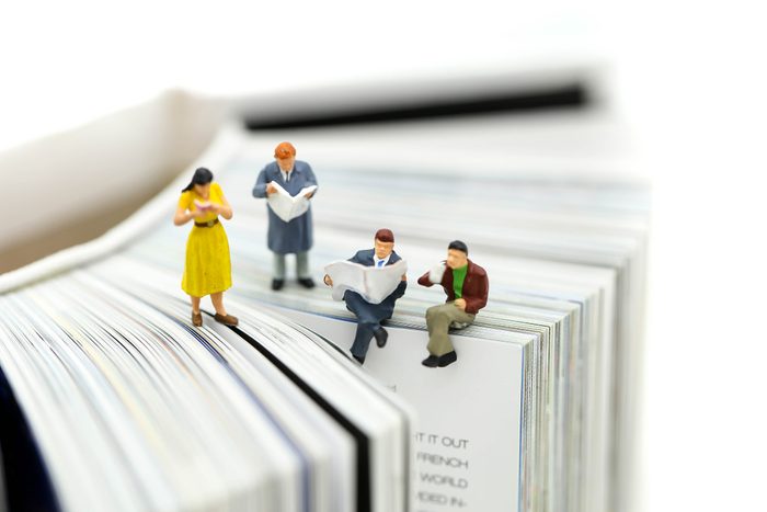 Miniature people: Businessman reading newspaper and sitting on book using as background education or business concept.
