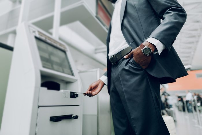 Close up of male is holding hand with watch in his pocket, while standing near cash dispenser