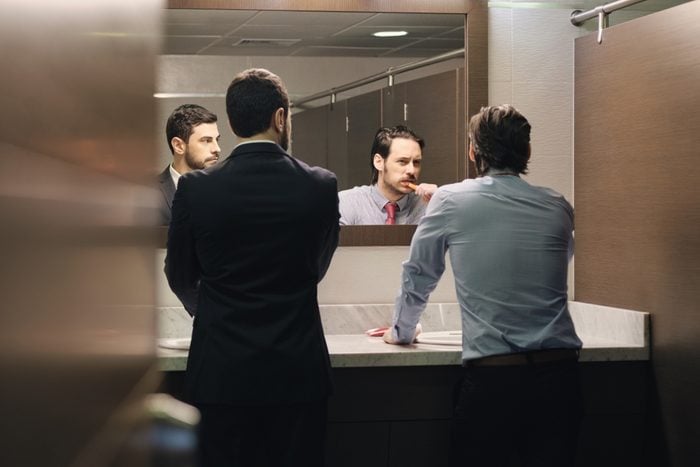 Business people in office bathroom. Young man using corporate restroom, washroom and lavatory. Public toilet in building with manager brushing teeth after lunch break