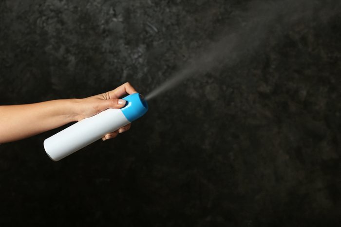 Woman spraying air freshener on dark background