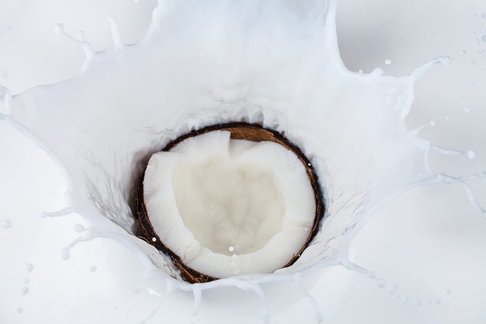 Half cut of coconut falling into milk splashes