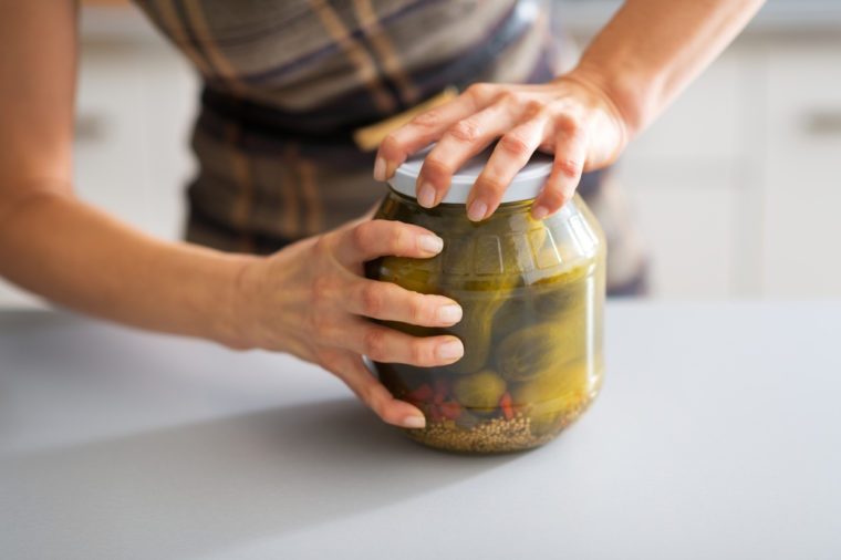 Closeup on young housewife opening jar of pickled cucumbers