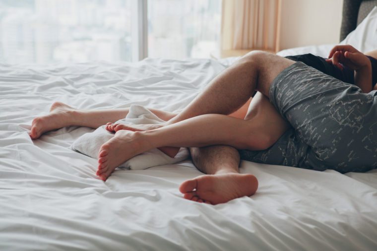 young sexy couple in love lying in bed in hotel, embracing on white sheets, close up legs, romantic mood