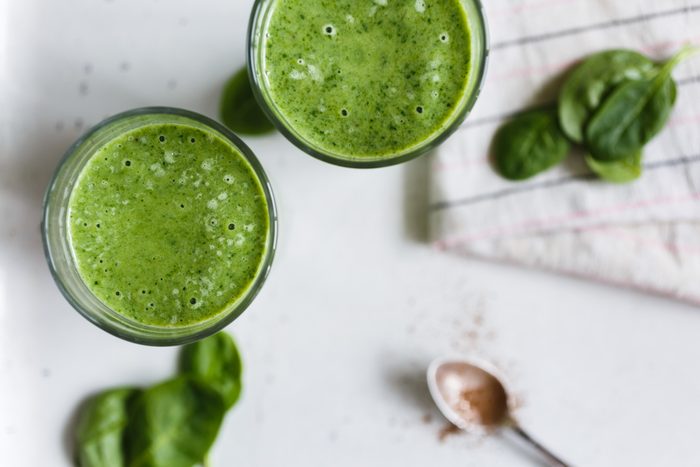 Two green smoothie with banana and spinach, fresh herbs on the background, top view