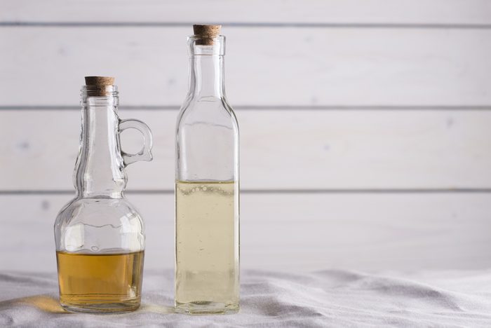 Transparent bottles with oil and vinegar on white wooden background.